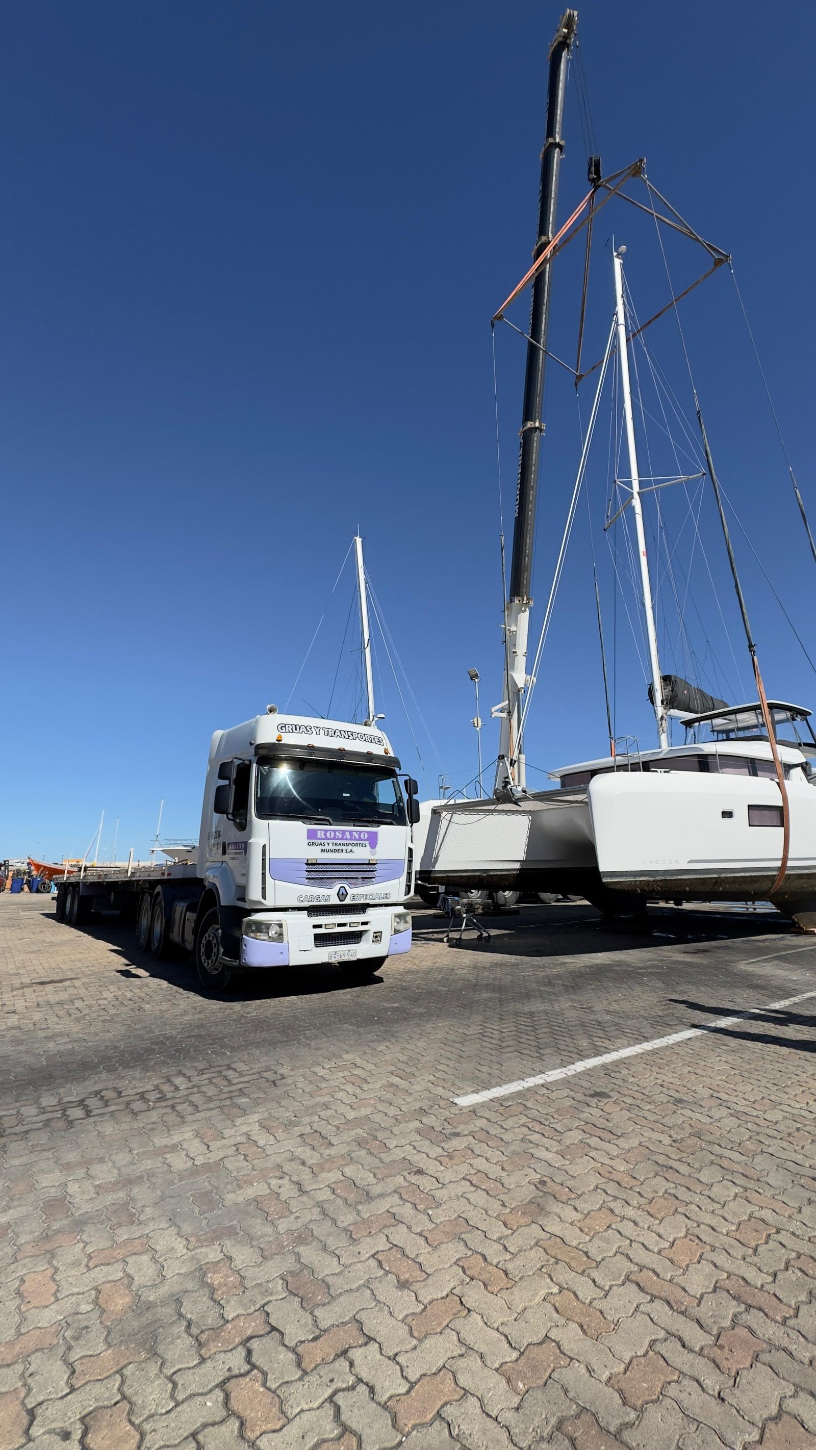 Camión con acoplado plataforma junto a veleros en el puerto