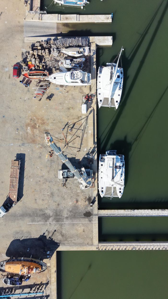 Vista aérea de muelle con veleros y grúa Rosano en operación de izaje, Uruguay